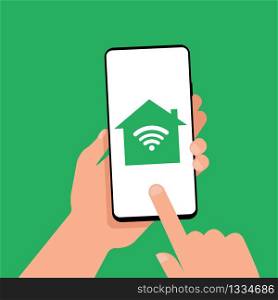 A hand is holding a smartphone with a smart home icon on the screen. Manage your home with your smartphone. Smart technology