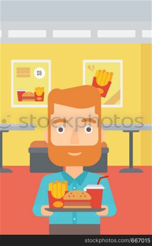 A hipster man with the beard holding a tray full of junk food on a cafe background vector flat design illustration. Vertical layout.. Man with fast food.