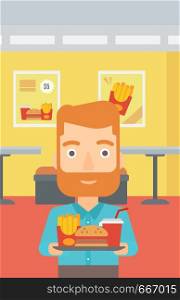 A hipster man with the beard holding a tray full of junk food on a cafe background vector flat design illustration. Vertical layout.. Man with fast food.