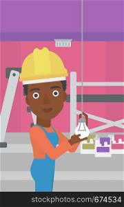 An african-american female worker twisting a light bulb on a background of room with paint cans and ladder vector flat design illustration isolated on white background. Vertical layout.. Electrician twisting light bulb.