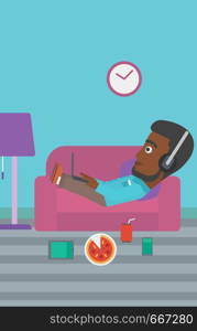 An african-american man in headphones lying on a sofa in living room with electronic devices and fast food vector flat design illustration. Vertical layout.. Man lying on sofa with many gadgets.