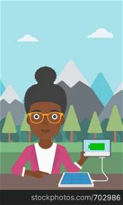 An african-american woman charging tablet computer with solar panel on a background of mountains. Charging digital tablet from portable solar panel. Vector flat design illustration. Vertical layout.. Solar panel charging tablet computer.