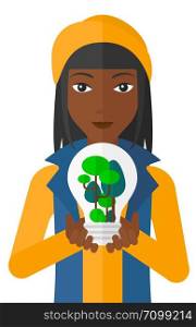 An african-american woman holding in hands a big lightbulb with trees inside vector flat design illustration isolated on white background. . Woman with lightbulb and trees inside.