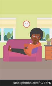An african-american woman lying on a sofa and watching tv with a remote control in her hand vector flat design illustration. Vertical layout.. Woman lying on sofa.