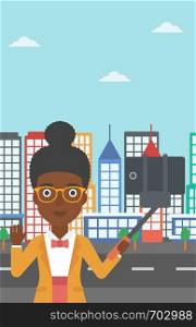 An african-american woman making selfie with a selfie-stick. An african-american woman taking photo with cellphone and waving on a city background. Vector flat design illustration. Vertical layout.. Woman making selfie vector illustration.