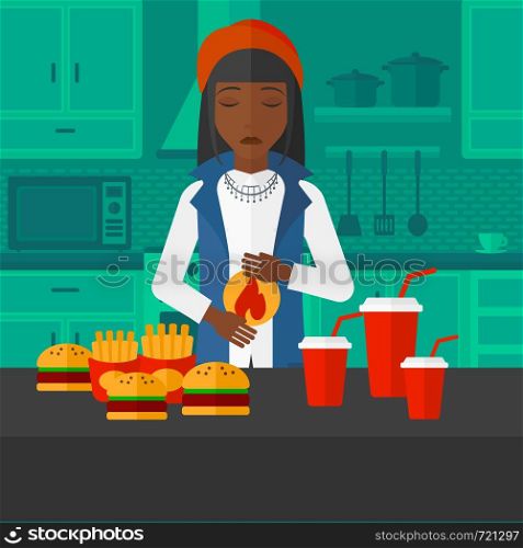 An african-american woman standing in front of table full of junk food and suffering from heartburn on a kitchen background vector flat design illustration. Square layout.. Woman suffering from heartburn.