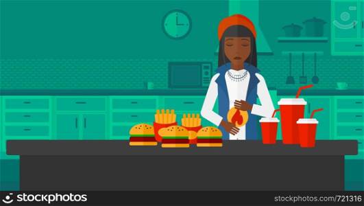 An african-american woman standing in front of table full of junk food and suffering from heartburn on a kitchen background vector flat design illustration. Horizontal layout.. Woman suffering from heartburn.