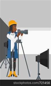 An african-american woman working with camera on the background of photo studio with lighting equipment vector flat design illustration. Vertical layout.. Photographer working with camera on a tripod.