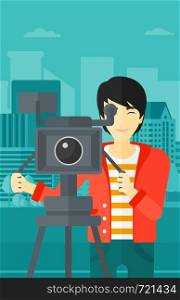 An asian cameraman with the beard looking through movie camera on a city background vector flat design illustration. Vertical layout.. Cameraman with movie camera on a tripod.