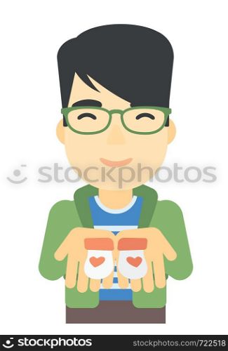 An asian man holding baby booties in hands vector flat design illustration isolated on white background. . Man holding baby booties.