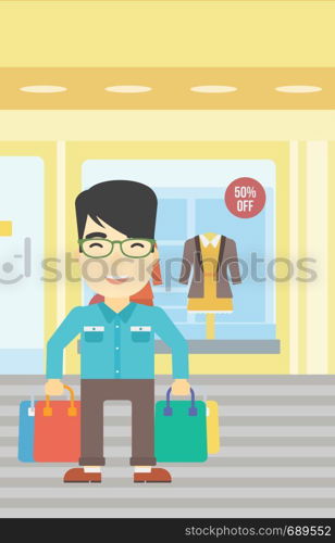 An asian man holding shopping bags on the background of boutique window with dressed mannequins. Happy young man carrying shopping bags. Vector flat design illustration. Vertical layout.. Happy man with shopping bags vector illustration.