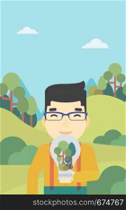An asian man standing on the background of green forest and holding in hands a big lightbulb with trees inside. Green energy concept. Vector flat design illustration. Vertical layout.. Man with lightbulb and trees inside.