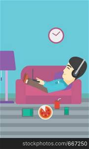 An asian man with belly relaxing on a sofa with many gadgets. Man lying on a sofa surrounded by gadgets. Man using gadgets at home. Vector flat design illustration. Vertical layout.. Man lying on sofa with many gadgets.
