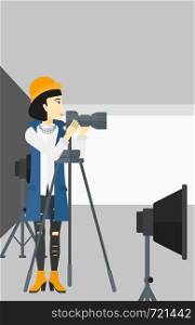 An asian photographer working with camera on the background of photo studio with lighting equipment vector flat design illustration. Vertical layout.. Photographer working with camera on a tripod.