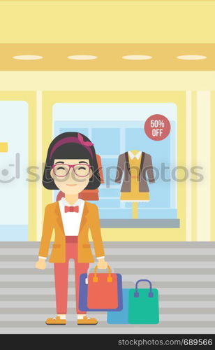 An asian woman holding shopping bags on the background of boutique window with dressed mannequins. Happy young woman carrying shopping bags. Vector flat design illustration. Vertical layout.. Happy woman with bags vector illustration.