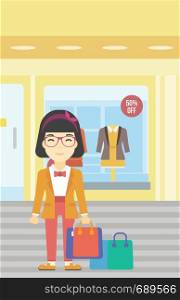 An asian woman holding shopping bags on the background of boutique window with dressed mannequins. Happy young woman carrying shopping bags. Vector flat design illustration. Vertical layout.. Happy woman with bags vector illustration.