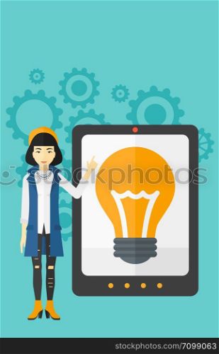 An asian woman pointing at a big tablet computer with a light bulb on a screen on a blue background with cogwheels vector flat design illustration. Vertical layout.. Woman pointing at tablet computer with light bulb on screen.