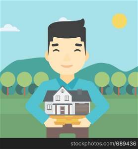 An asian young man holding house model in hands on the background of mountains. Real estate agent with house model. Vector flat design illustration. Square layout.. Man holding house model vector illustration.