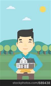 An asian young man holding house model in hands on the background of mountains. Real estate agent with house model. Vector flat design illustration. Vertical layout.. Man holding house model vector illustration.