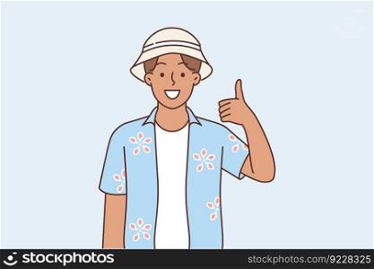 Asian man in summer shirt and tourist hat showing thumbs up calling to visit songkran festival in Thailand. Tanned man traveling in asian countries shows approving gesture to praise travel company. Asian man in summer shirt showing thumbs up calling to visit songkran festival in Thailand