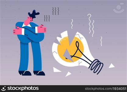 Business crisis and default concept. Young sad frustrated businessman cartoon character standing looking at broken huge light bulb vector illustration . Business crisis and default concept.