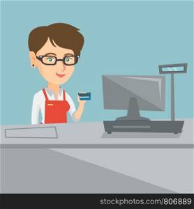 Caucasian smiling cashier standing at the checkout and holding a credit card. Young cashier making payment by credit card. Cashier showing a credit card. Vector cartoon illustration. Square layout.. Young caucasian cashier holding a credit card.