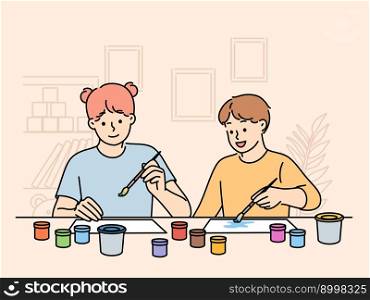Children sit at table doing joint creativity draw pictures using watercolor or gouache. Boy and girl with brushes in their hands participate in kids creativity competition. Children sit at table doing joint creativity draw pictures using watercolor or gouache