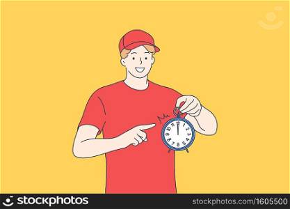 Courier delivery service, being in time concept. Happy young man in red working uniform standing and pointing at alarm clock meaning delivering parcel in time for client on yellow background. Courier delivery service, being in time concept