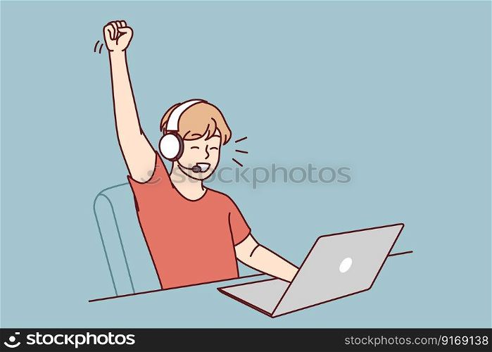 Delighted teen boy sitting at table with laptop playing video game and defeating virtual opponents. Schoolboy in headphones makes victory gesture overjoyed at broken record in internet game . Delighted teen boy sitting at table with laptop playing video game and defeating virtual opponents