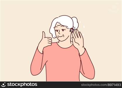 Elderly woman uses hearing aid and shows thumbs up confirming good sound volume thanks to new device. Gray-haired old lady with hearing aid enjoys opportunity to hear others and communicate freely . Elderly woman uses hearing aid and shows thumbs up confirming good sound volume thanks to new device
