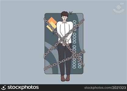 Financial crisis and debts concept. Young stressed man being locked with chains to huge credit card having debts as slave over grey background . Financial crisis and debts concept