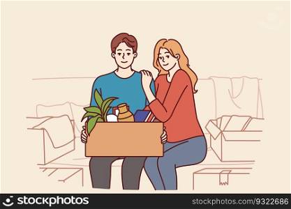Happy couple is sitting on couch with cardboard box after moving into new house or buying own apartment. Family of man and woman smile happy about renting property in elite area and moving. Happy couple is sitting on couch with cardboard box after moving or buying own apartment
