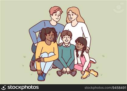 Happy family couple with multiracial children sitting together on lawn in park and smiling looking at camera. Man and woman with adopted children rejoice in presence of large family. Happy family couple with multiracial children sitting together on lawn in city park
