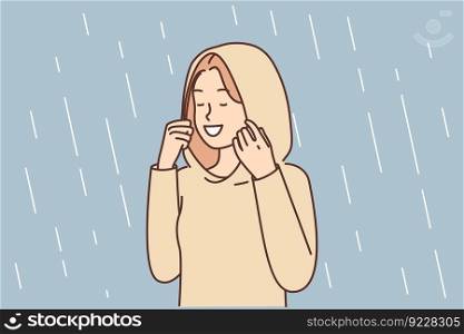 Happy woman enjoys autumn rain standing in autumn raincoat with hood that protects against drops. Positive girl relish spring weather and precipitation with storm rain after long drought. Happy woman enjoys autumn rain standing in autumn raincoat with hood that protects against drops