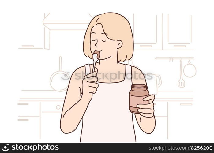 Happy woman stands in kitchen with jar of chocolate paste or peanut butter and licks spoon satisfying hunger with junk food. Positive girl eats high-calorie peanut butter after long diet. Happy woman stands in kitchen with jar of chocolate paste or peanut butter and licks spoon