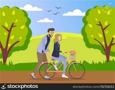 Happy young man is helping a smiling woman to ride a bicycle on the road at summer forest background. Girl is riding a pink bicycle with a bouquet of flowers in a basket. Romantic ride in the park. Happy young man is helping a smiling woman to ride a bicycle on the road at summer forest background