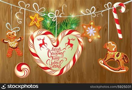 Holiday greeting Card with xmas gingerbread, candy and fir-tree branches. Hand written calligraphic text Merry Christmas and Happy New Year on wooden background.