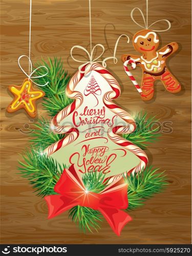 Holiday greeting Card with xmas gingerbread - man and star cartoons, candy and fir-tree branches. Hand written calligraphic text Merry Christmas and Happy New Year on wooden background.