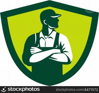 Illustration of an organic farmer wearing hat and overalls arms folded looking to the side viewed from front set inside shield crest on isolated background done in retro style.