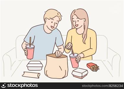 Man and woman have lunch sitting at table enjoy takeout food delivered by courier from restaurant. Guy and girl consume fast food and cold drinks, not wanting to spend time preparing dinner . Man and woman have lunch sitting at table enjoy takeout food delivered by courier from restaurant