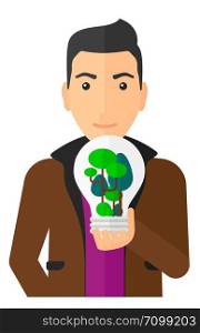 Man holding in hands a big lightbulb with trees inside vector flat design illustration isolated on white background. Vertical layout.. Man with lightbulb and trees inside.