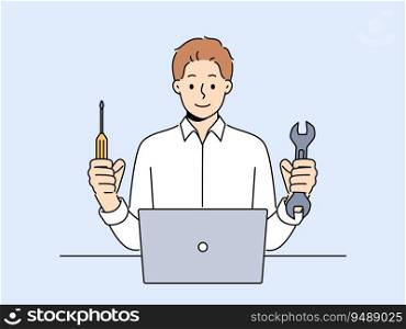 Man repairs laptop after breakdown and holds screwdriver and wrench in hands, working as system administrator. Guy fixes laptop or wants to upgrade by replacing hard drive of computer. Man repairs laptop after breakdown and holds screwdriver and wrench, working as system administrator