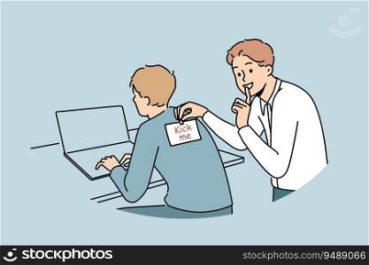 Man sticks kick me sticker on back of colleague working with laptop to make prank and laugh. Cheerful student guy jokes with friend and asks others not to talk about uplifting prank. Man sticks kick me sticker on back of colleague working with laptop to make prank and laugh