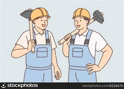 Men in builders uniforms and hardhats hold sledgehammers to demolish wall of emergency building or redevelopment. Guys builders are ready to work on construction site or in renovated room. Men in builders uniforms and hardhats hold sledgehammers to demolish wall of emergency building 