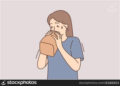 Nervous girl breathes into paper bag trying to cope with panic attack caused by psychological disorder. Little teenage girl experiencing panic and mental problems needs help of psychotherapist. Nervous girl breathes into paper bag trying to cope with panic caused by psychological disorder