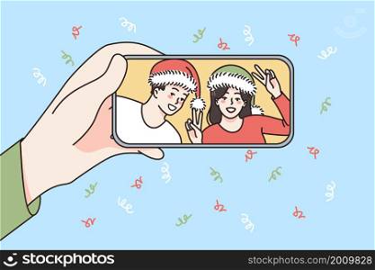 Online New Year celebration concept. Human hand holding smartphone with smiling couple in Santa hats celebrating and greeting online vector illustration . Online New Year celebration concept