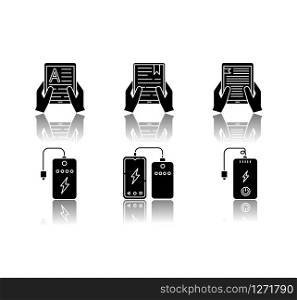 Portable electronic devices drop shadow black glyph icons set. Power bank. Portable battery. Pocket charging gadget. Hands holding e-readers, tablets. Isolated vector illustrations on white space