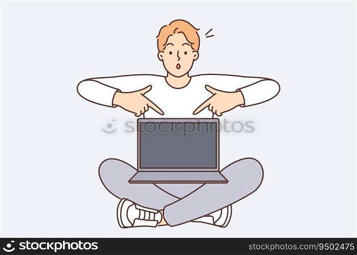 Shocked man with laptop pointing fingers at screen recommending visiting interesting website or downloading software. Guy sits with laptop on knees offering to buy cool computer at bargain price. Shocked man with laptop pointing fingers at screen recommending visiting interesting website