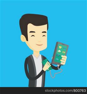 Smiling asian man recharging his smartphone with mobile phone portable battery. Young man holding a mobile phone and battery power bank. Vector flat design illustration. Square layout.. Man reharging smartphone from portable battery.