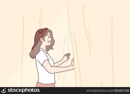 Smiling woman looks out window opening curtains and enjoying rays of summer morning sun. Girl opens curtains rejoicing at new sunny day after waking up in morning or dreams of going for walk. Smiling woman looks out window opening curtains and enjoying rays of summer morning sun